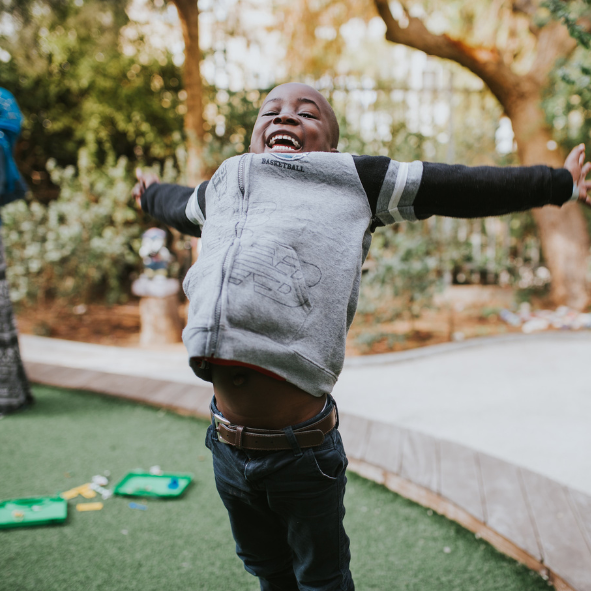 A Black boy in a gray hoodie with navy sleeves jumping. 